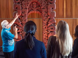 A tour guide in a blue shirt explains facts about a statue to a group at a museum.