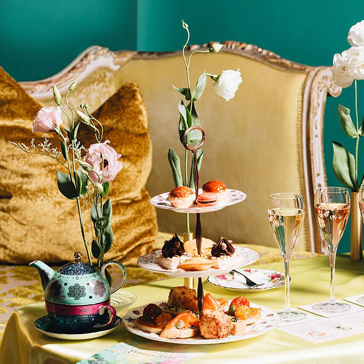 A table full of high tea offerings including cake stands full of finger food, champagne glasses and a tea pot.