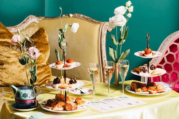 A table full of high tea offerings including cake stands full of finger food, champagne glasses and a tea pot.