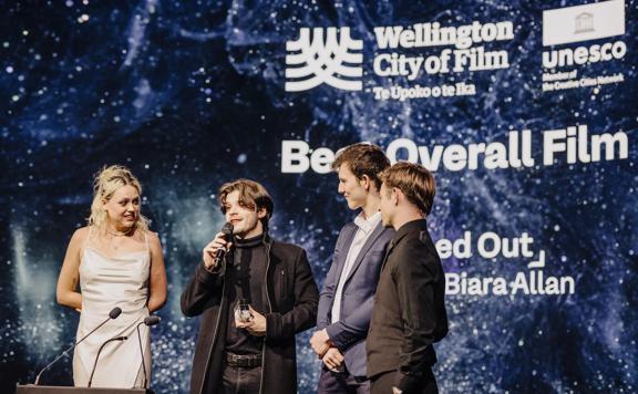 Lola McLeod-Riera, Flynn Biara Allen and two other people stand together on stage and accept the Best Overall Film award at the New Zealand Youth Film Festival.