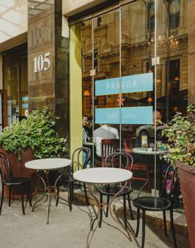 The exterior of Pravda Cafe & Grill. Large planters sit beside the doors, and small tables and chairs outside.