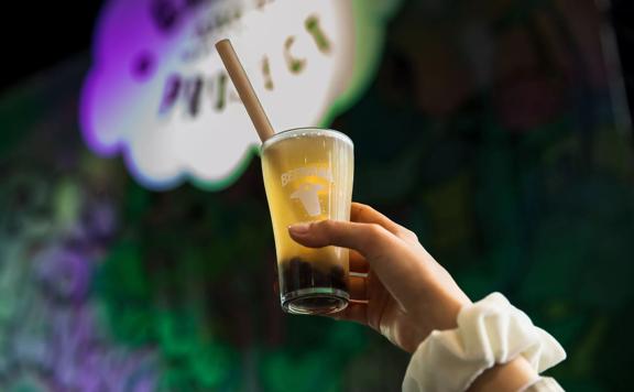 Upwards angle of a hand holding a glass of boba beer in the air with Beervana logo on glass.