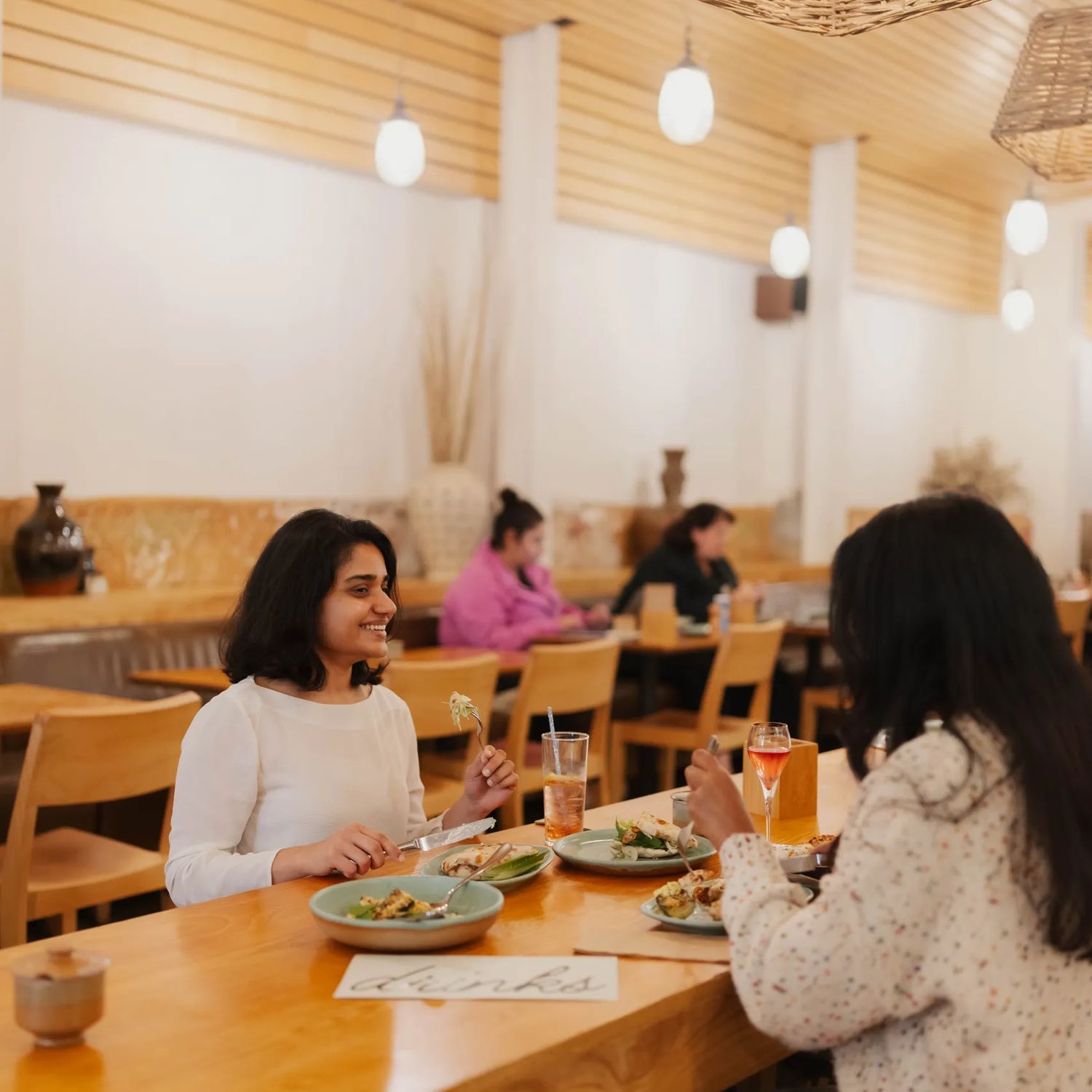 Two customers dining at Loretta on Cuba Street. One smiles at the other as they eat.