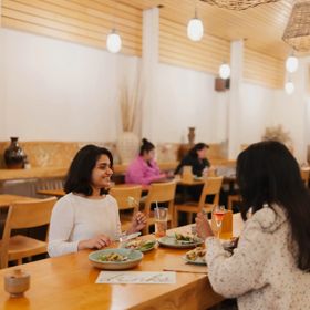 Two customers dining at Loretta on Cuba Street. One smiles at the other as they eat.