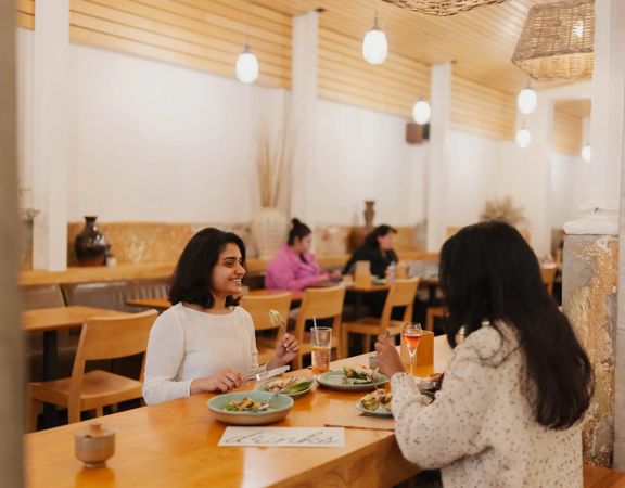 Two customers dining at Loretta on Cuba Street. One smiles at the other as they eat.