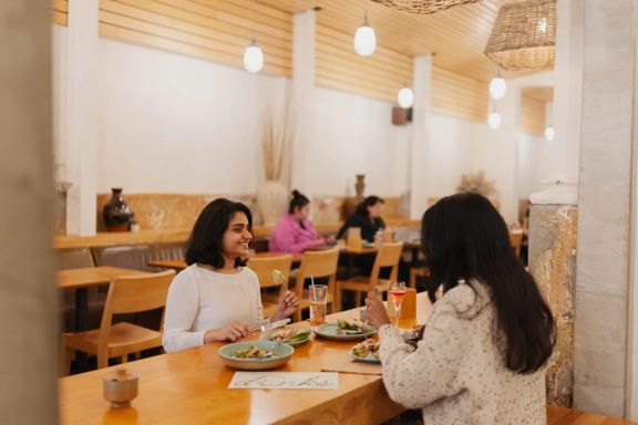 Two customers dining at Loretta on Cuba Street. One smiles at the other as they eat.