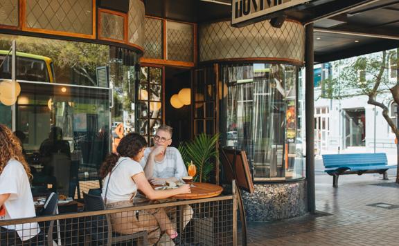 A couple sits at a small table on the patio enjoying cocktails and food.