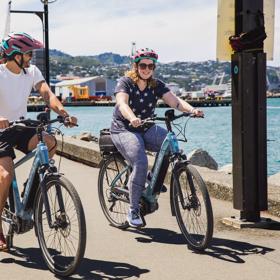 Two cyclists wear helmets while riding e-bikes along Wellington's waterfront.