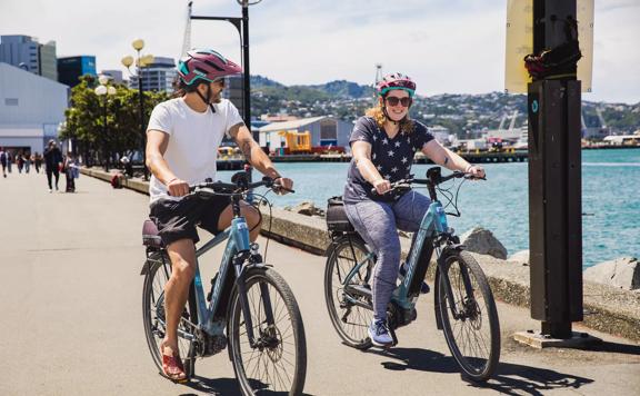 Two cyclists wear helmets while riding e-bikes along Wellington's waterfront.