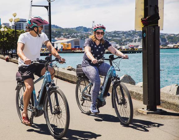 Two cyclists wear helmets while riding e-bikes along Wellington's waterfront.