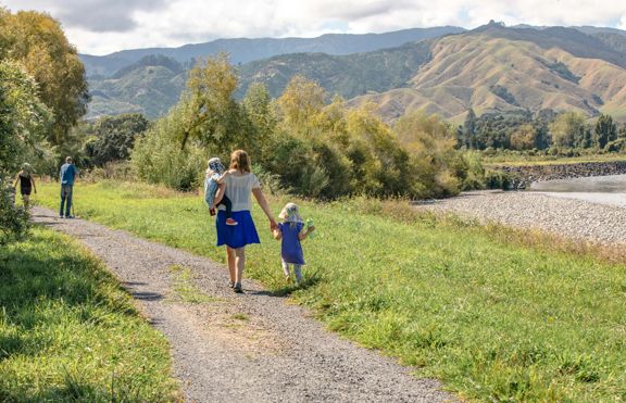 An adult and two children walk along a path in a lush valley with mountains in the background.