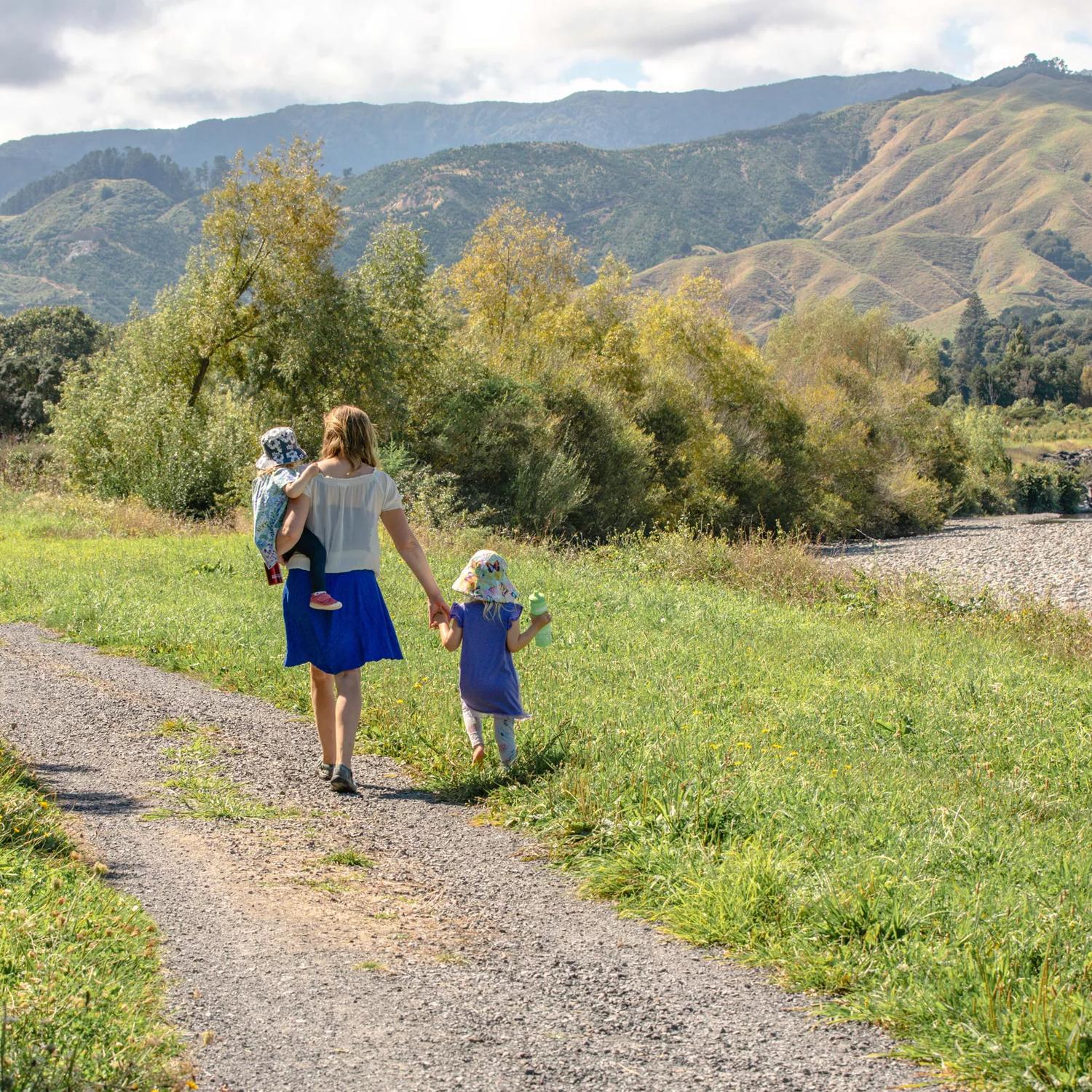 An adult and two children walk along a path in a lush valley with mountains in the background.