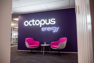 The interior of octopus energy Wellington headquarters, with 2 bright pink chairs under a neon sign.