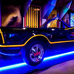 A replica 1966 Batmobile. A thin yellow line traces the contours of the black car’s body. A bright blue neon light glows beneath. 