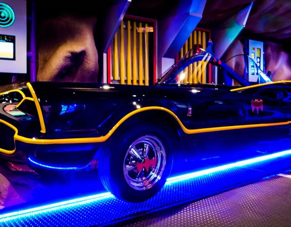 A replica 1966 Batmobile. A thin yellow line traces the contours of the black car’s body. A bright blue neon light glows beneath. 