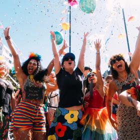Joyful CubaDupa Festival attendees wear colourful outfits and throw confetti in the air.
