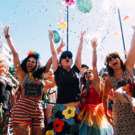Joyful CubaDupa Festival attendees wear colourful outfits and throw confetti in the air.