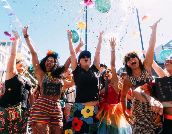 Joyful CubaDupa Festival attendees wear colourful outfits and throw confetti in the air.