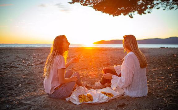 Two people enjoy fish and chips at Raumati Beach during Sunset.