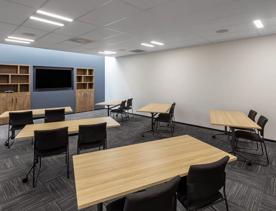 Inside a conference room in Oaks Wellington hotel, where 6 tables each with 2 chairs, face towards a tv.