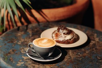 A flat white and a cinnamon roll on a table.