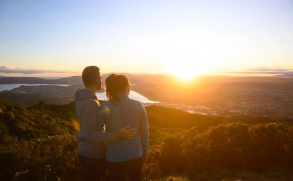 Two people stand arm in arm looking at a picturesque sunset from Rangituhi/Colonial Knob Walkway.