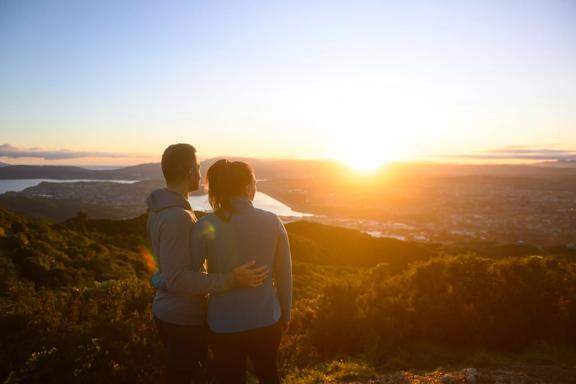 Two people stand arm in arm looking at a picturesque sunset from Rangituhi/Colonial Knob Walkway.