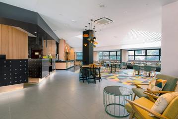 Dining room inside Atura Hotel, tables, chairs and couches on the right with a bar and kitchen on the left.