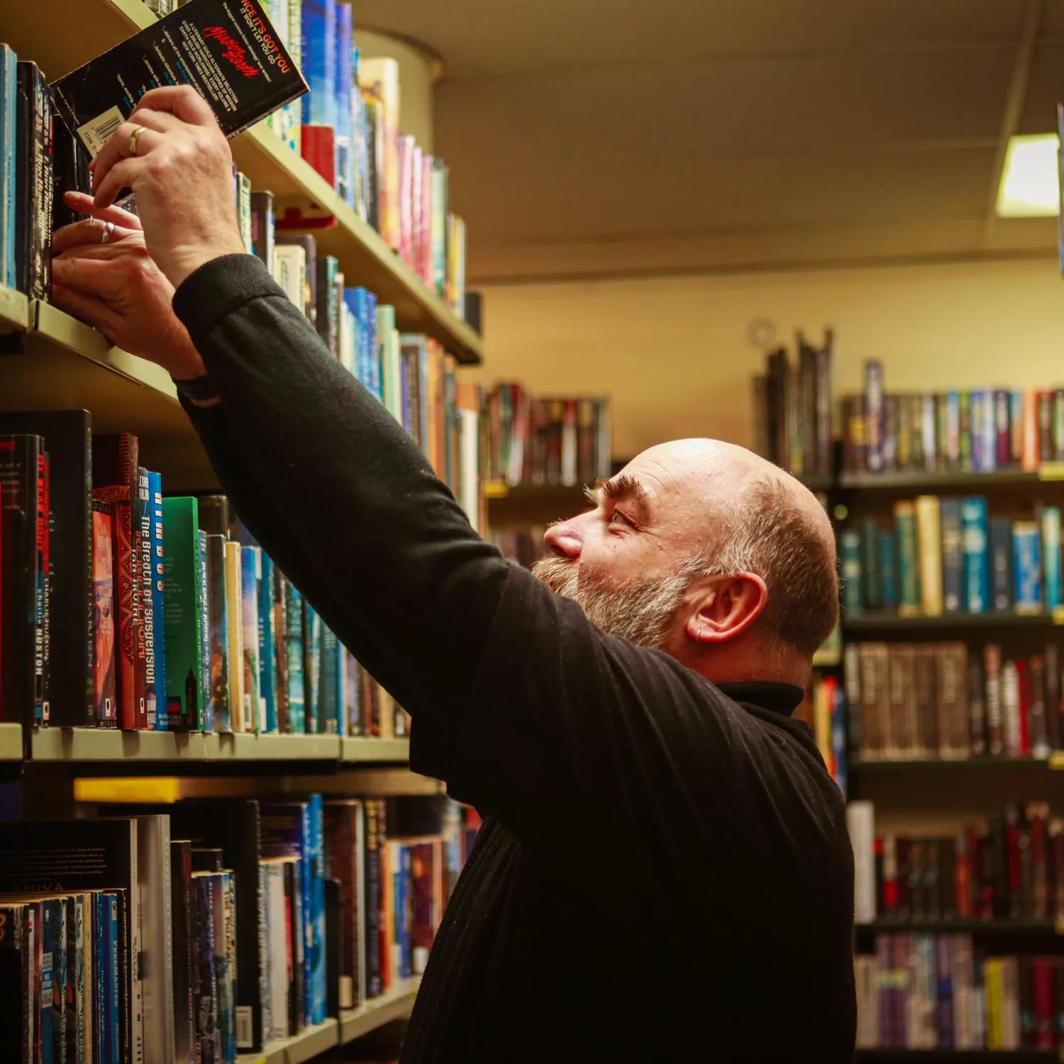 Person at Arty Bees Books in Wellington placing a book back into a shelf full of books.