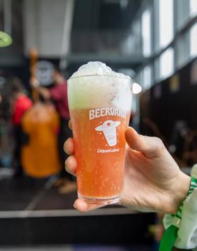 Close-up of a hand holding up a Beervana glass filled with an orange drink and foam atop.