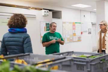 Person in green Kaibosh shirt talking to 2 others with blurred out food in foreground.