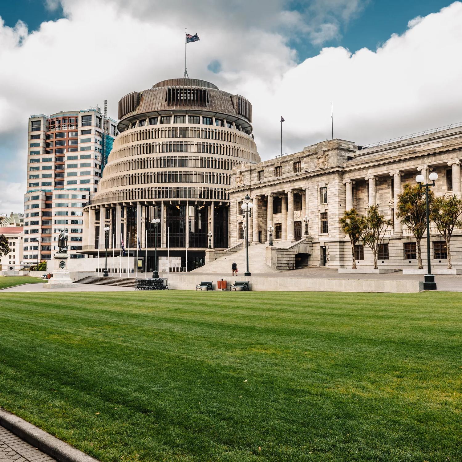 The New Zealand Parliament building in located at 1 Museum Street in Wellington with a grassy lawn in front.