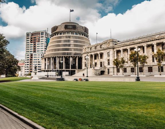 The New Zealand Parliament building in located at 1 Museum Street in Wellington with a grassy lawn in front.