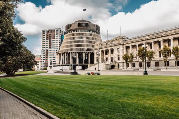 The New Zealand Parliament building in located at 1 Museum Street in Wellington with a grassy lawn in front.