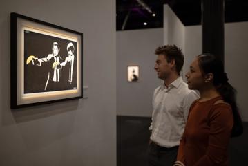 Two people look at Banksy's 'Pulp Fiction' screen print displayed at The Art of Banksy exhibition at Tākina in Wellington.