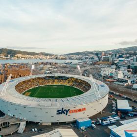 A drone shot of Sky Stadium with the city behind it at sunset. The stadium is full of fans.