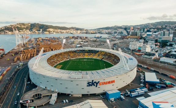 A drone shot of Sky Stadium with the city behind it at sunset. The stadium is full of fans.