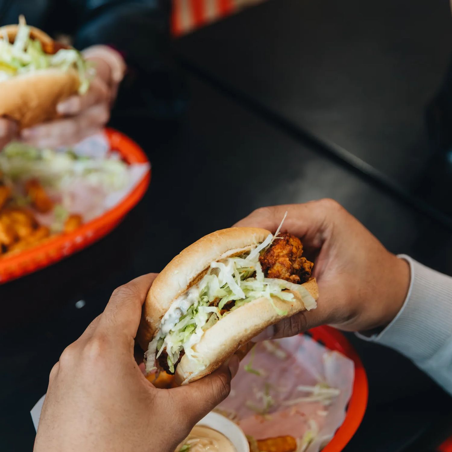 Two sets of hands holding chicken burgers with lettuce, and fries.