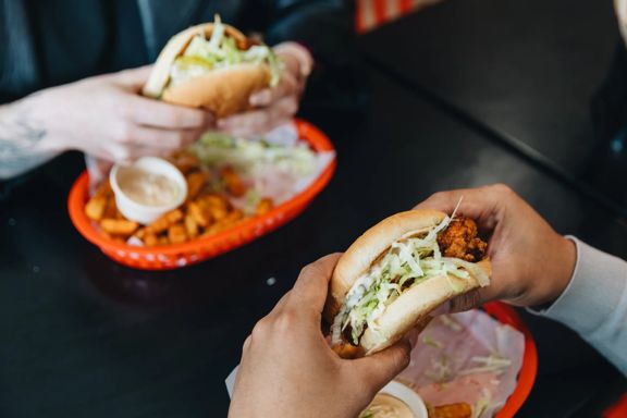 Two sets of hands holding chicken burgers with lettuce, and fries.
