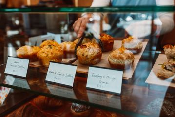 A worker uses tongs to pick up a ham and cheese scone-muffin.