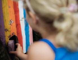 young child opens a tiny wooden door of the fairy house in Horoeka Scenic reserve.