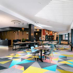 The lobby of Atura Hotel, with tables and a colourfully patterned carpet.