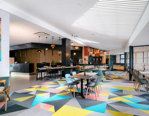 The lobby of Atura Hotel, with tables and a colourfully patterned carpet.