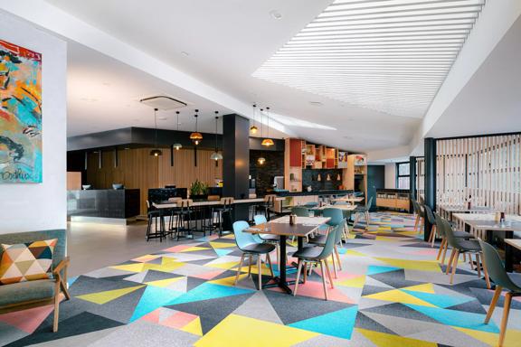 The lobby of Atura Hotel, with tables and a colourfully patterned carpet.