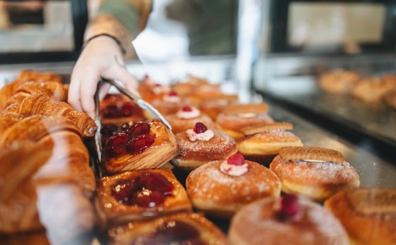A person uses tongs to pick up a plum danish from a pastry window.