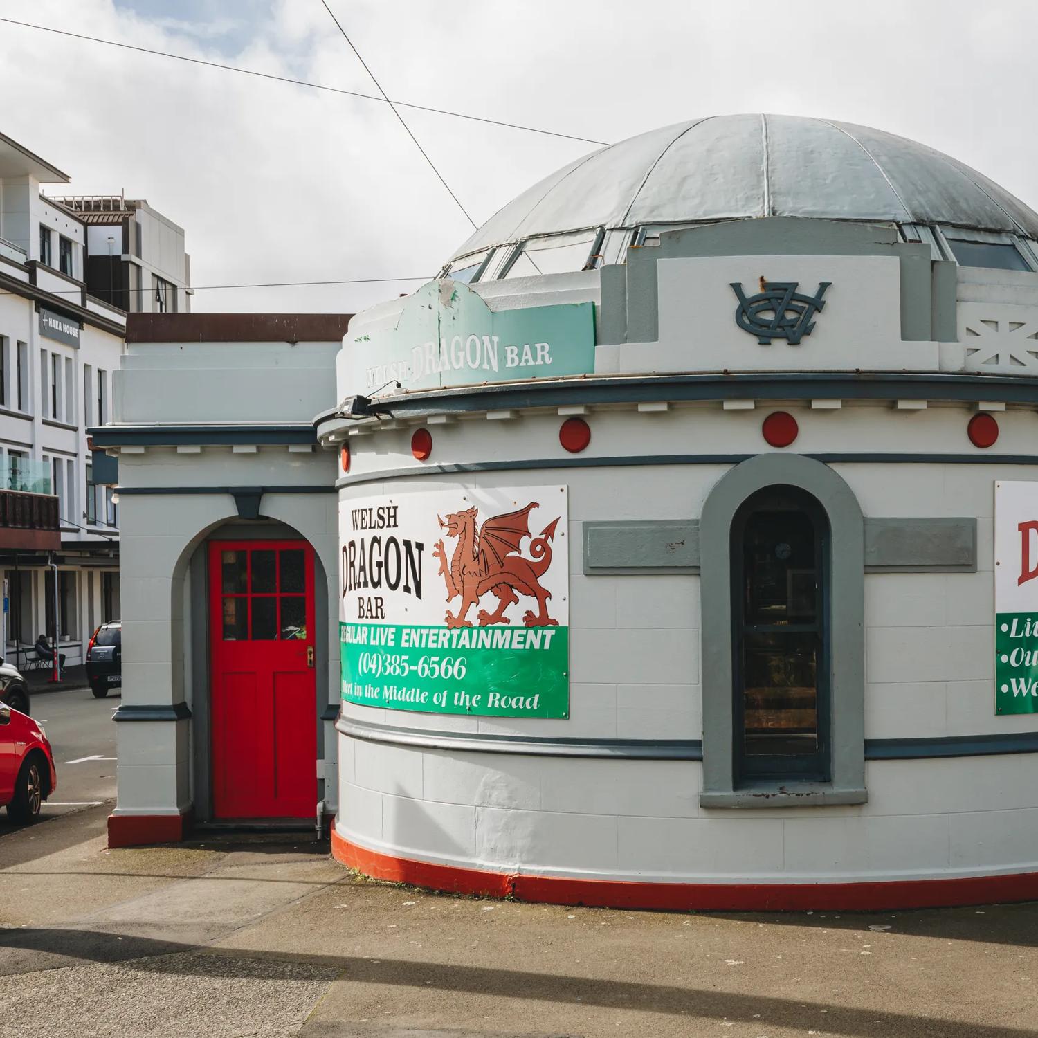 The exterior of The Welsh Dragon Bar, a pub set inside a former public toilet on Cambridge Terrace in Wellington. The building has a circular dome with two red doors on either side. 