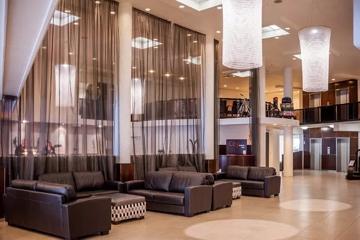 West Plaza Hotel lounge and lobby space with high ceilings, cylindrical chandeliers and leather couches in a seating area.