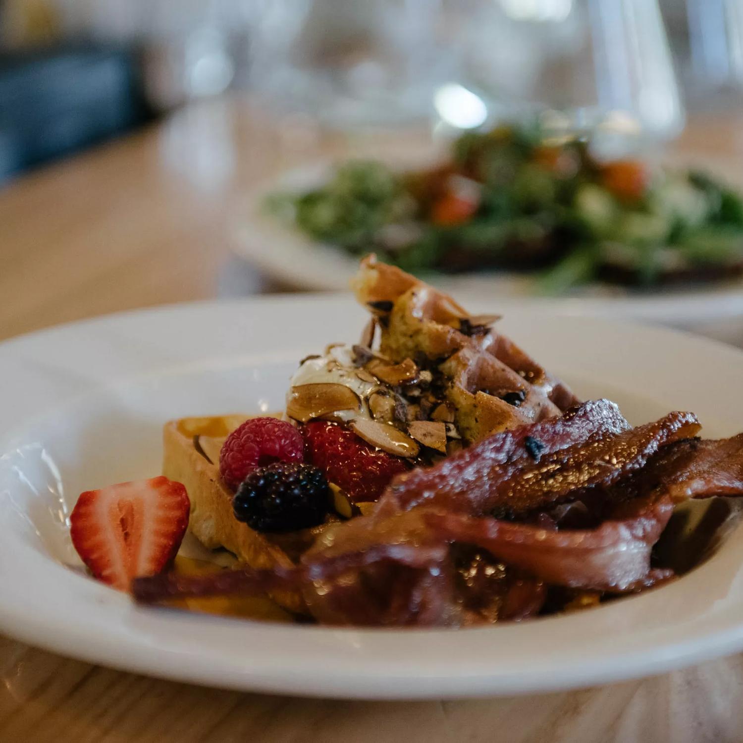 Waffles with berries, syrup and bacon strips on a white plate. The dish is from Prefab Eatery, a restaurant in Te Aro Wellington.