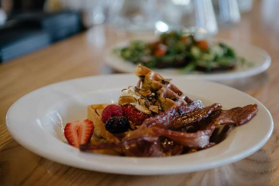 Waffles with berries, syrup and bacon strips on a white plate. The dish is from Prefab Eatery, a restaurant in Te Aro Wellington.