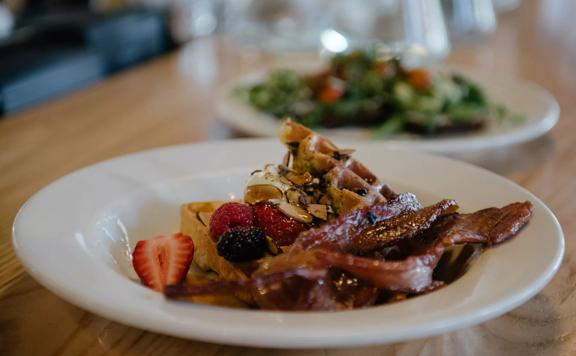 Waffles with berries, syrup and bacon strips on a white plate. The dish is from Prefab Eatery, a restaurant in Te Aro Wellington. 